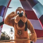 Playful Pluto character waving during a sunny Orlando parade at an amusement park.